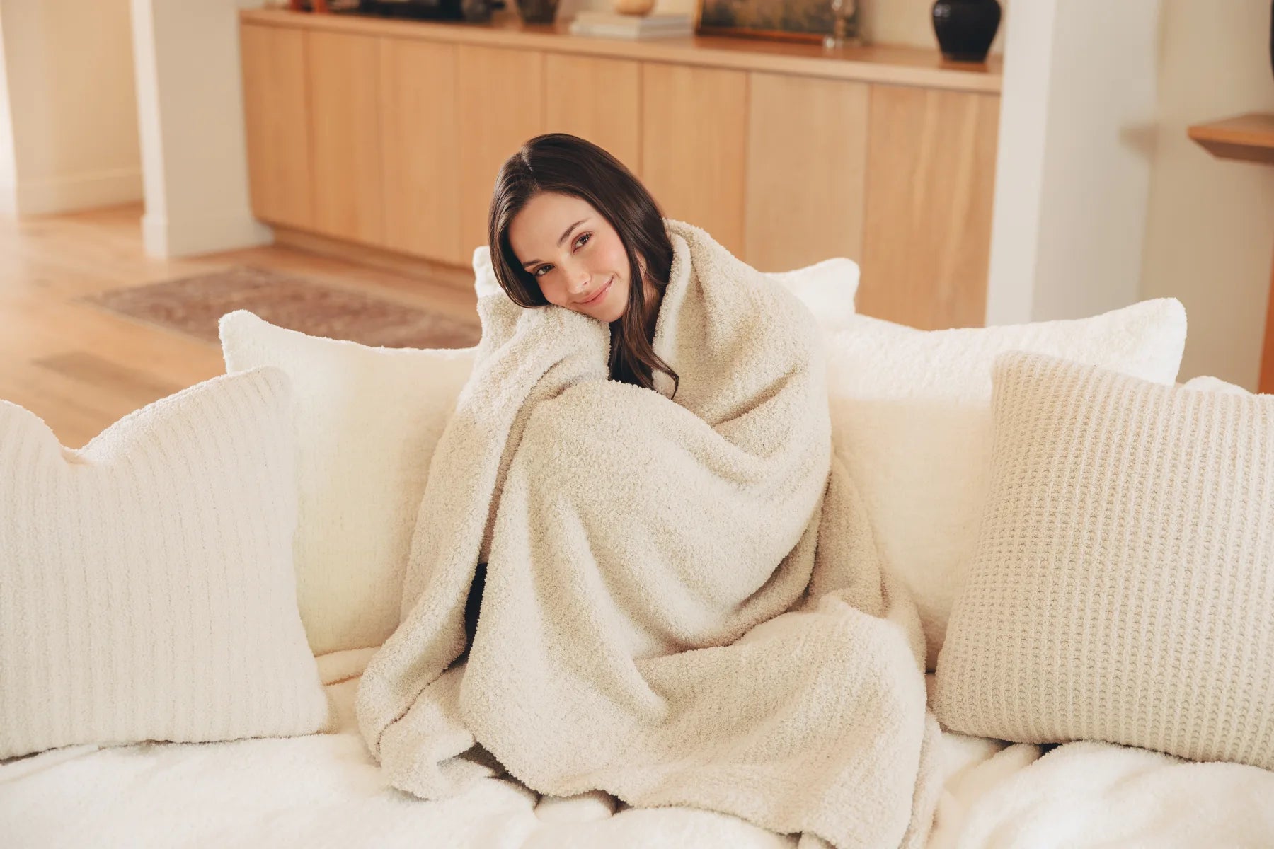 A woman relaxing on a sofa with a Kashwére throw and soft pillows