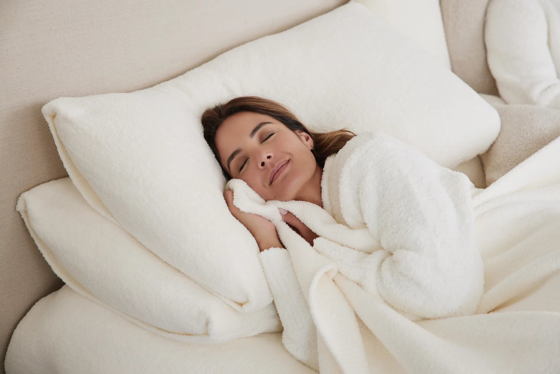 A woman resting among Kashwére pillows and soft white bedding